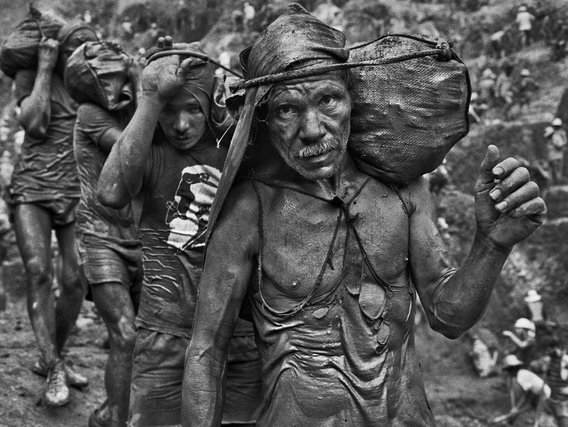 Mineiros carregados com sacos caminham por uma trilha.